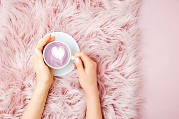 Female hands holding a cup of coffee on the fluffy fur plaid.  Flat lay, top view