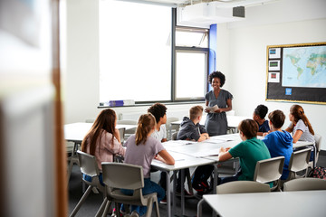 Female High School Tutor Standing By Table With Students Teaching Lesson