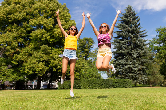 leisure, people and friendship concept - happy teenage girls or friends jumping and having fun at summer park