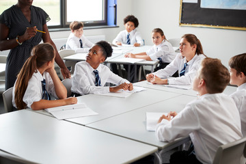 Detail Of Female High School Tutor Helping Students Wearing Uniform Seated Around Tables In Lesson