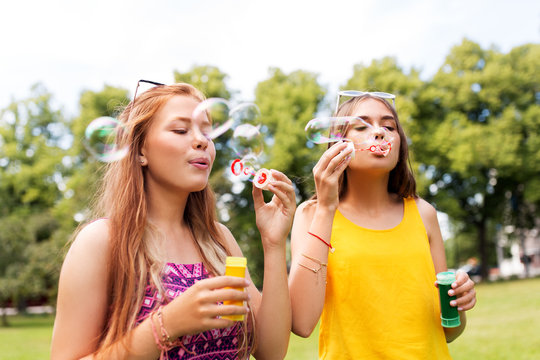 leisure and friendship concept - happy teenage girls or friends blowing bubbles at summer park