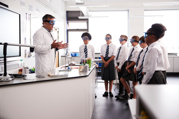 Male High School Tutor Teaching High School Students Wearing Uniforms In Science Class