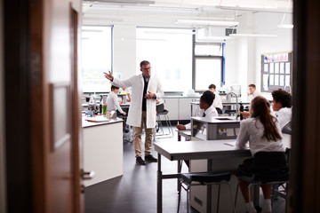 Male High School Tutor Teaching High School Students Wearing Uniforms In Science Class