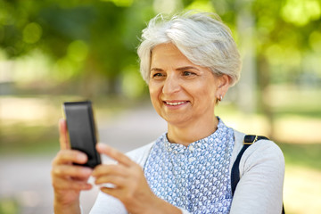 old age, retirement and technology concept - happy senior woman photographing by smartphone summer park