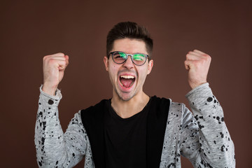 Obraz premium Happy positive excited young man clenching fists and screaming, wearing casual t-shirt glad to hear good news, celebrating his victory or success. Life achievement, goals and happiness concept.