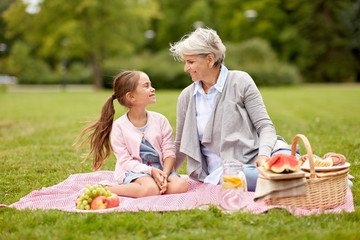 family, leisure and people concept - happy grandmother and granddaughter having picnic at summer park