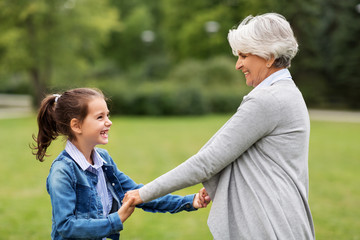 family, leisure and people concept - happy grandmother and granddaughter playing game or dancing at summer park