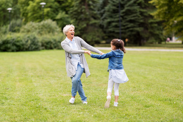 family, leisure and people concept - happy grandmother and granddaughter playing game or dancing at...