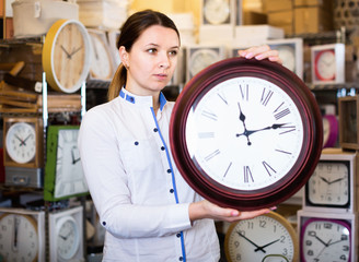 Woman is choosing new clock for her home in the store.