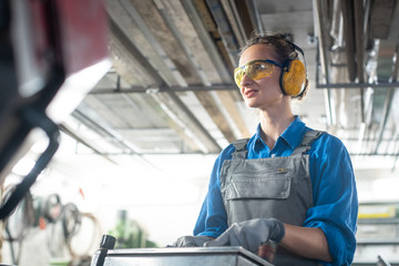 Woman worker operating a machine tool in metal workshop or factory in a diligent manner