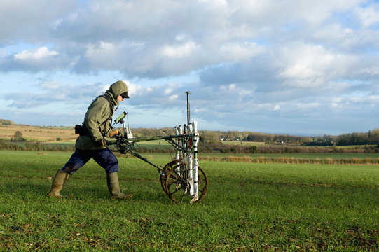A geophysicist pushing a trolley with ground mapping sensors, creating a geophysical survey of the subsoil in a field. 