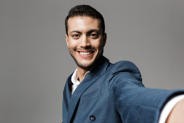 Excited happy business man take a selfie posing isolated over grey wall background.