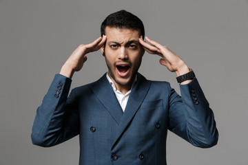 Fototapeta premium Aggressive screaming business man with headache posing isolated over grey wall background.