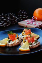 Christmas background with smoked salmon canapes on crackers over black plate