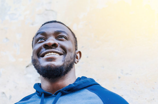 Portrait of a cheerful positive black guy close-up in a sports sweater against a light wall background. Race issues. City photo, space. Youthful culture.