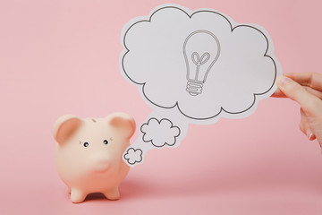Hand say cloud with lightbulb, idea near piggy money bank isolated on pastel pink wall background. Money accumulation, investment, banking services, wealth concept. Copy space advertising mock up.
