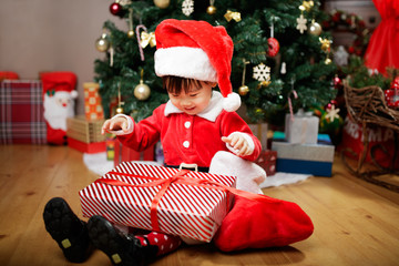 toddler baby girl wearing santa claus costume open gift box  in front of christmas tree