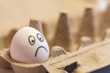 lonely white egg with a sad painted face in a cardboard box