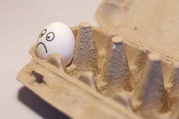 lonely white egg with a sad painted face in a cardboard box