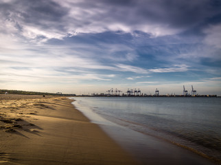 Long empty clean sand Stogi beach in Gdansk, Poland with Stalin shipyard with cranes in the background - obrazy, fototapety, plakaty
