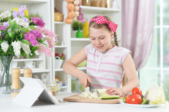 Cute girl preparing delicious fresh salad in kitchen