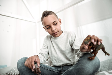 Dinosaur age. Pleasant young boy holding a dinosaur toy while playing with it