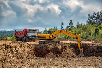 Yellow excavator and empty truck working at the construction site © EdVal