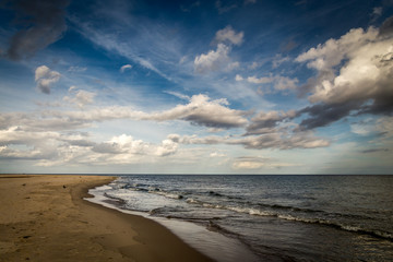 Long empty sand beach on Hel peninsula in Poland with dramatic, cloudy blue sky
