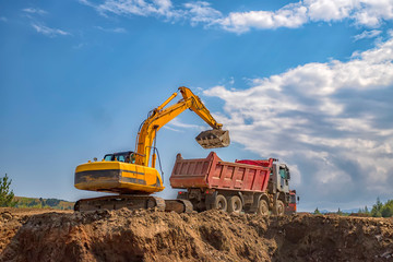 Yellow excavator and empty dump truck working at the construction site - Powered by Adobe