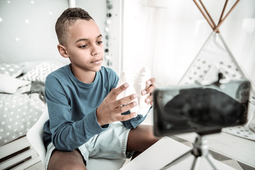 Young scientist. Pleasant smart boy holding a dinosaur skull model while recording a video for his...