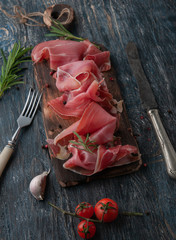 still life with proshutto. depicted in various angles with the addition of ingredients. Oil, olives, cheese, tomatoes, rosemary. Serving on a dark wooden table