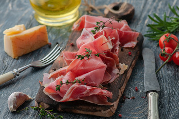 still life with proshutto. depicted in various angles with the addition of ingredients. Oil, olives, cheese, tomatoes, rosemary. Serving on a dark wooden table