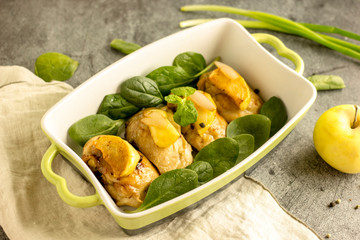 Slices of fried chicken with apples in a baking dish with greens on a dark stone background