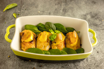 Slices of fried chicken with apples in a baking dish with greens on a dark stone background