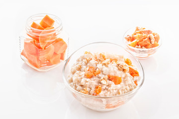 Fototapeta na wymiar Oatmeal with pumpkin and nuts in a glass plate and sliced carrots in a jar on a white background. Close-up.