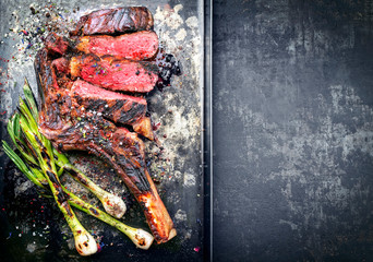 Barbecue dry aged wagyu tomahawk steak with leek as top view on a black metal sheet with copy space