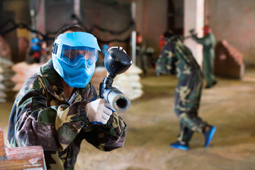 Portrait of blue team player who is aiming in opponents on paintball field.