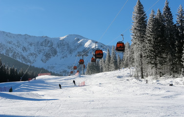 Cableway cabins and skiers on a sunny day on the slopes of the Jasna ski resort.