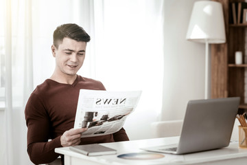 My newspaper. Positive delighted male person sitting at the table and looking at interesting article