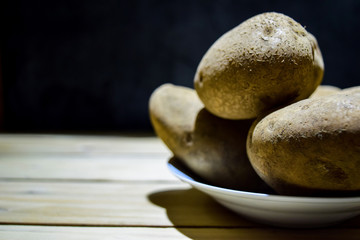 Fototapeta na wymiar Close-up Fresh potatoes lying on wooden boards on Black background.