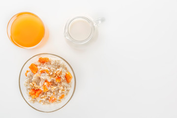Oatmeal with pumpkin and nuts, a glass of fresh juice and a jug of milk on a white background. Top view. Copy space.
