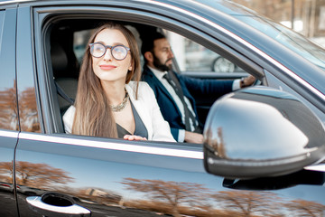 Elegant businesswoman looking out the window driving luxury car with businessman in the city