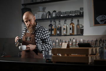 Brutal young barista in an apron makes coffee at the bar in a modern cafe