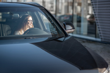 Young businesswoman driving a luxury car, view from the outside through the windshield