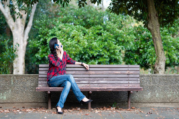 Obraz premium 公園のベンチでスマートフォンを操作する女性