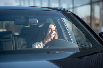 Young businesswoman driving a luxury car, view from the outside through the windshield - Powered by Adobe