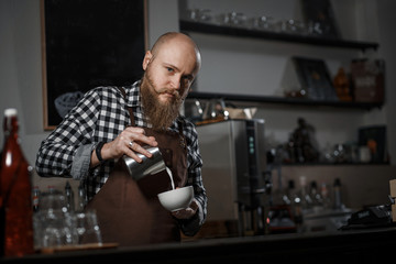 Brutal young barista in an apron makes coffee at the bar in a modern cafe
