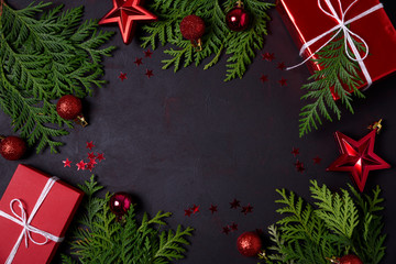 Christmas frame of red gift boxes, fir branches, confetti and toys on black background. Flat lay. Top view. Copy space