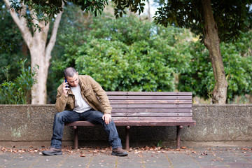 公園のベンチでスマートフォンを操作する男性