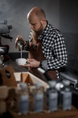 Brutal young barista in an apron makes coffee at the bar in a modern cafe